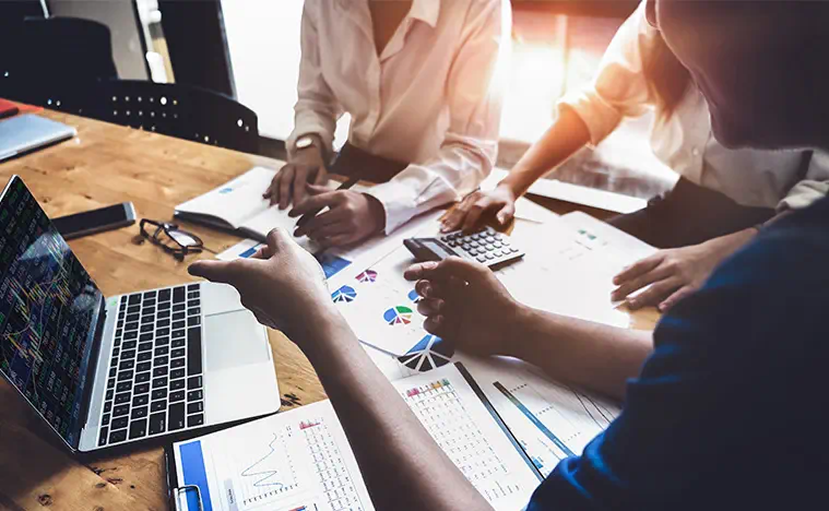 Business people looking over scattered reports and using a calculator.