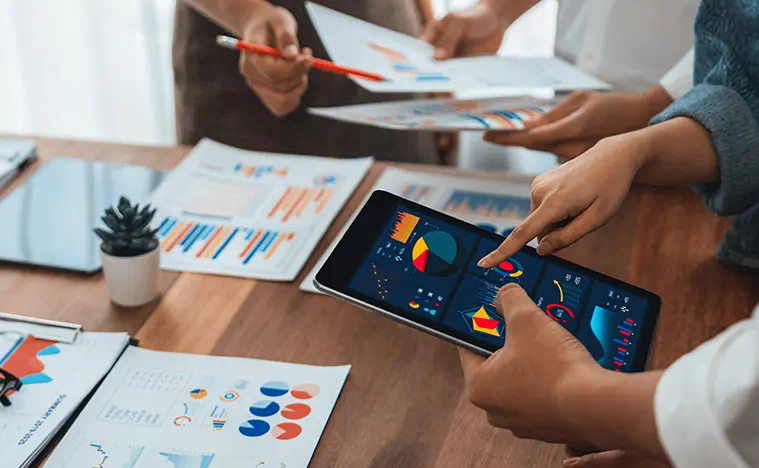 Three business people look over financial reports printed and on a tablet.