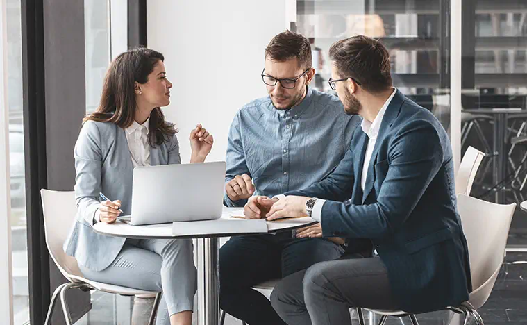 Three business people meet in a modern office lobby.