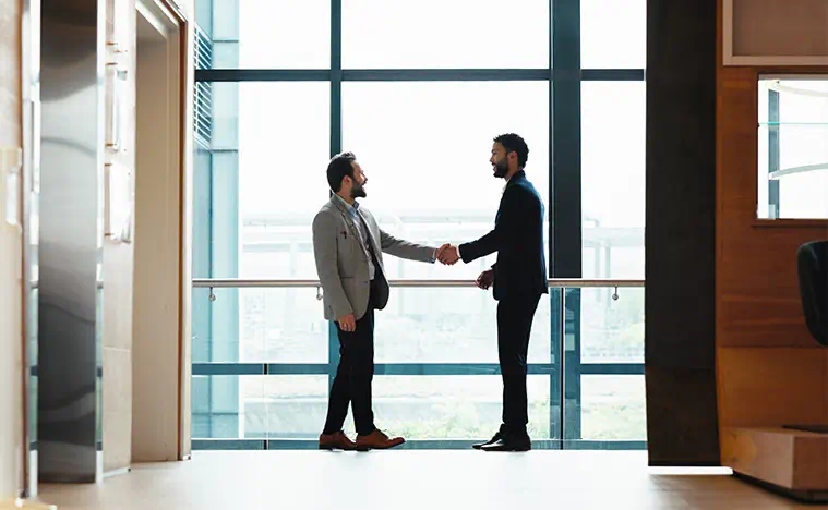 Two business men shaking hands in an office lobby.