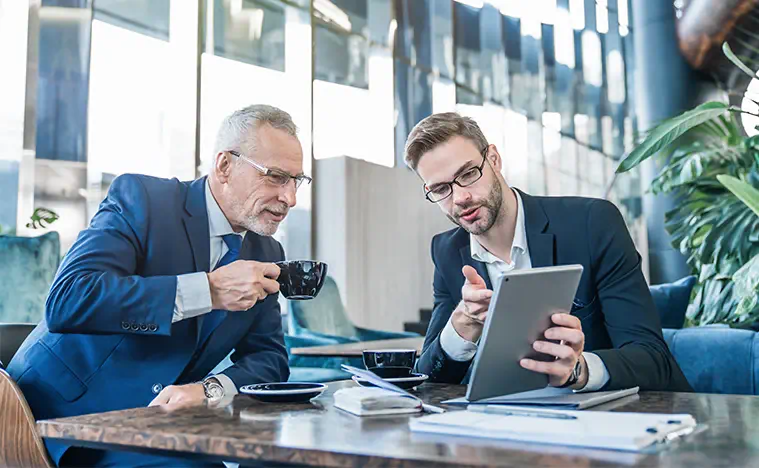 About Us – Listen First Two business men looking over a report in a modern meeting room.