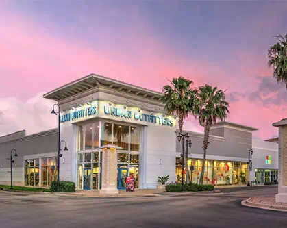 A retail shop lit up at night, sunset in the background.
